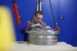 Arbeiter mit Schutzbrille, der in einer Industrie­werkstatt sorgfältig eine große, hängend gelagerte Metallkomponente montiert oder inspiziert.